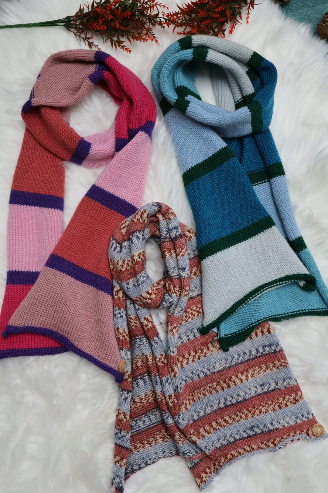 Colorful knitted scarves on a white surface with a plant.