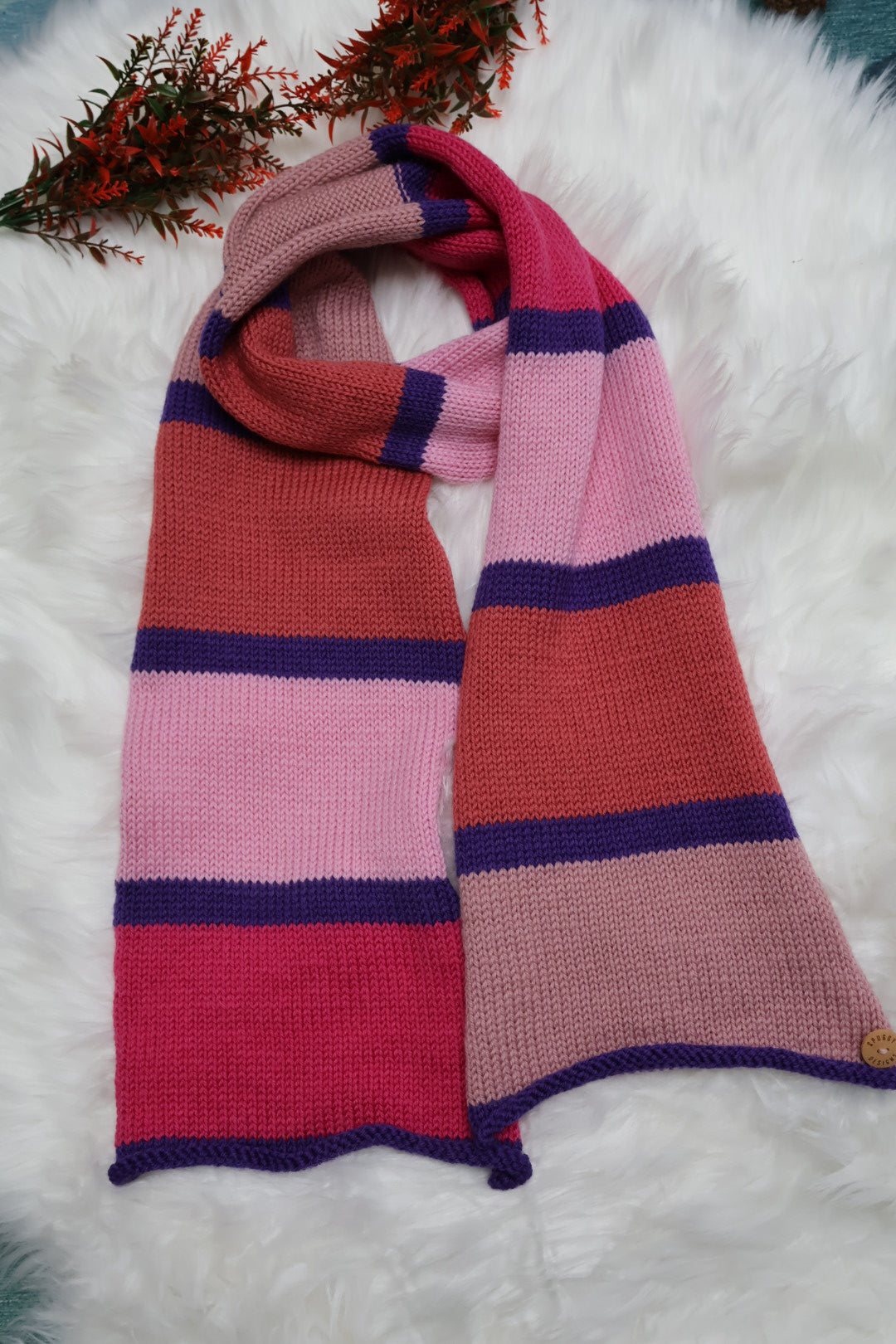Striped pink and purple scarf on a white fluffy surface with a small plant.
